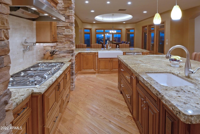 kitchen featuring exhaust hood, stainless steel gas stovetop, pendant lighting, and sink