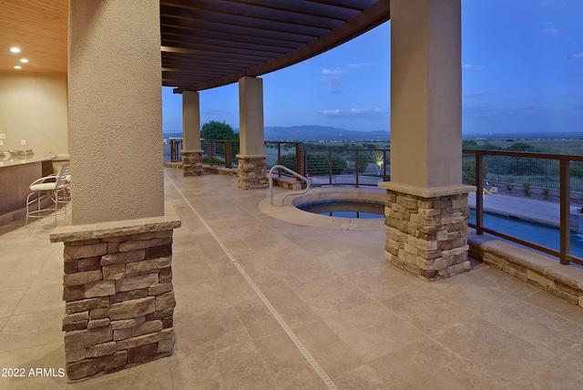 patio terrace at dusk featuring a mountain view, a community hot tub, and a pergola