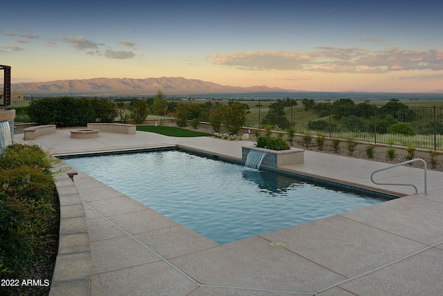 pool at dusk featuring pool water feature, a mountain view, and a patio