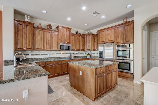 3660 S Golden Eye Ln, Gold Canyon, AZ 85118 - kitchen with a kitchen island, appliances with stainless steel finishes, arched walkways, a sink, and brown cabinetry