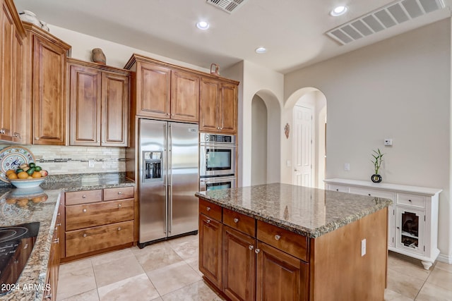 3660 S Golden Eye Ln, Gold Canyon, AZ 85118 - kitchen with stainless steel appliances, decorative backsplash, dark stone counters, arched walkways, and brown cabinetry