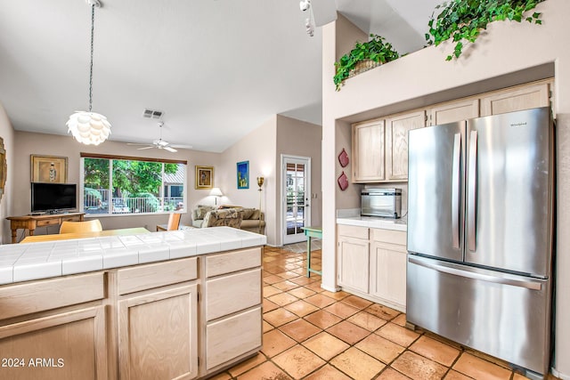 kitchen with lofted ceiling, light tile patterned floors, stainless steel refrigerator, tile countertops, and light brown cabinets