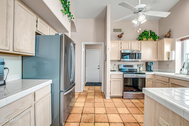 kitchen with stainless steel appliances, sink, tile countertops, and light brown cabinetry