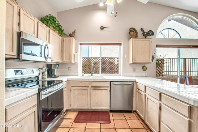 kitchen featuring lofted ceiling, sink, appliances with stainless steel finishes, tile counters, and a healthy amount of sunlight