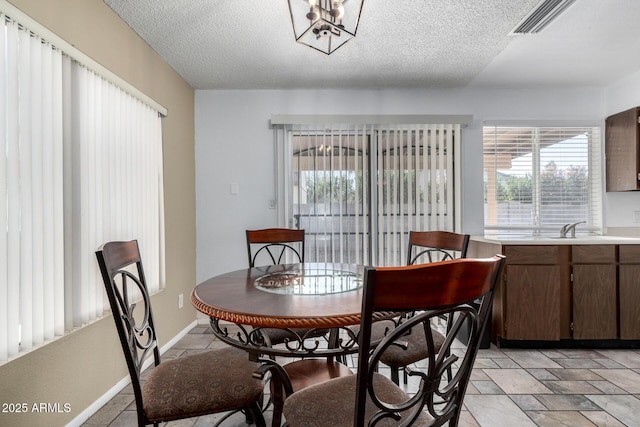 dining area featuring sink, a chandelier, and a textured ceiling