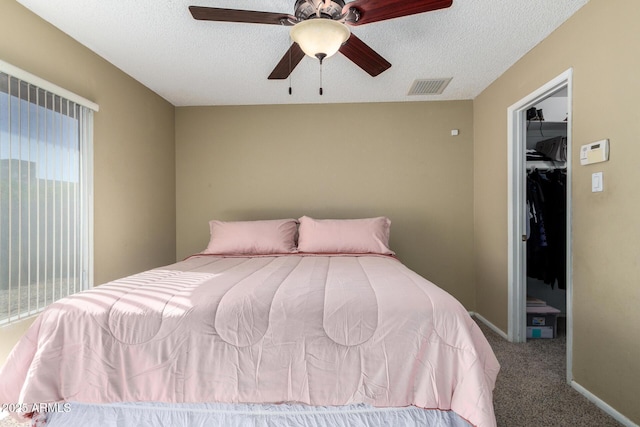 bedroom featuring ceiling fan, carpet floors, a textured ceiling, a walk in closet, and a closet