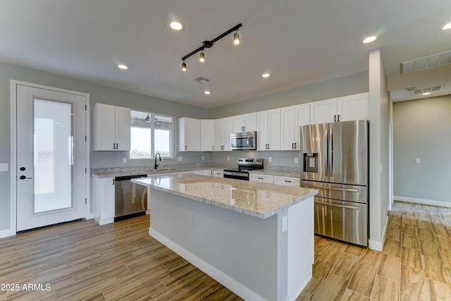 22009 W Montgomery Rd, Wittmann, AZ 85361 - kitchen with stainless steel appliances, a sink, a center island, white cabinets, and light wood finished floors