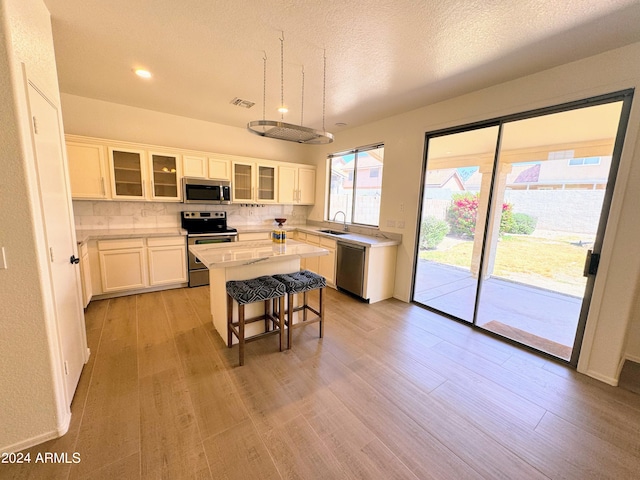 kitchen with white cabinets, appliances with stainless steel finishes, a center island, light wood-type flooring, and a kitchen bar