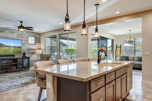 kitchen featuring a center island with sink, ceiling fan with notable chandelier, light tile floors, and pendant lighting