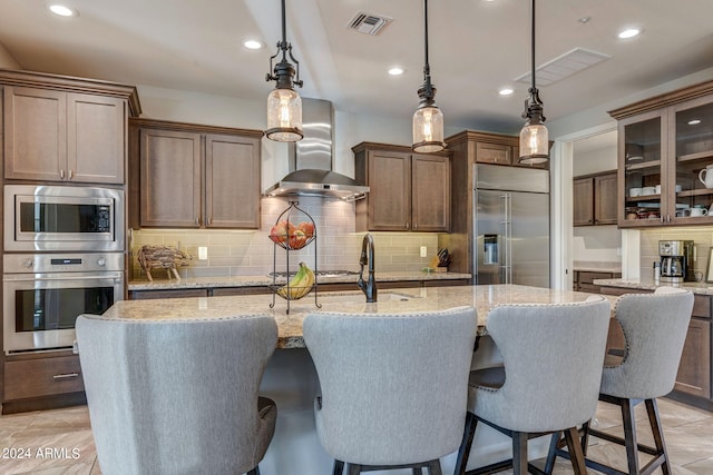 kitchen with tasteful backsplash, built in appliances, and wall chimney range hood