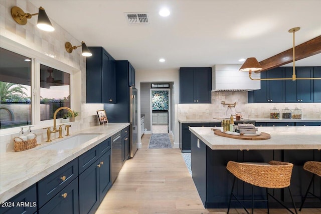 kitchen with blue cabinetry, light hardwood / wood-style flooring, decorative backsplash, and sink