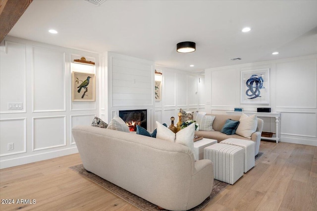 living area featuring visible vents, light wood-style flooring, a decorative wall, and a glass covered fireplace