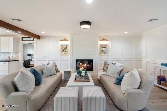 living area with a glass covered fireplace, a decorative wall, recessed lighting, and visible vents
