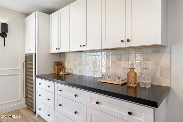 kitchen with wine cooler, light wood-type flooring, backsplash, dark countertops, and white cabinets
