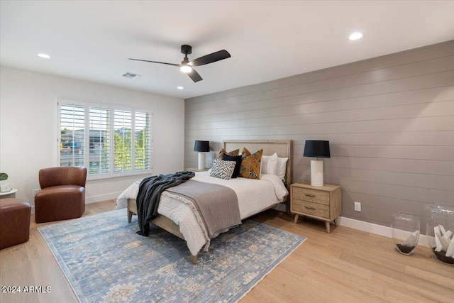 bedroom with wooden walls, light hardwood / wood-style floors, and ceiling fan