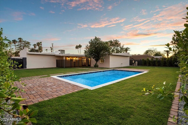 pool at dusk featuring fence, an outdoor pool, a yard, and a patio area