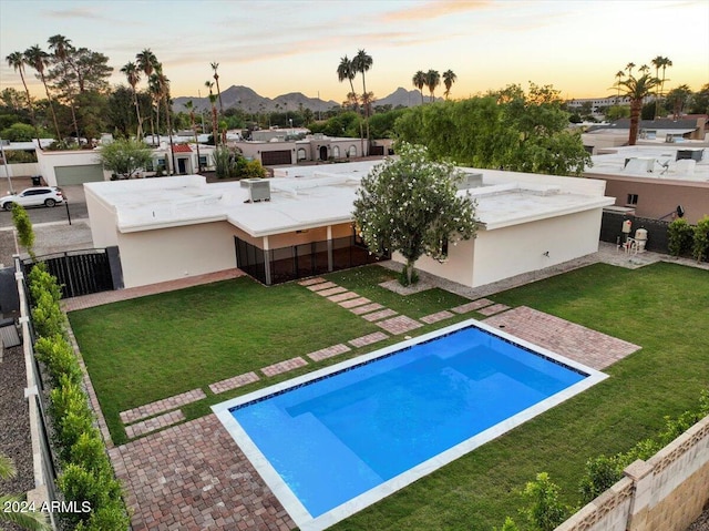 pool at dusk with a patio, a mountain view, and a yard