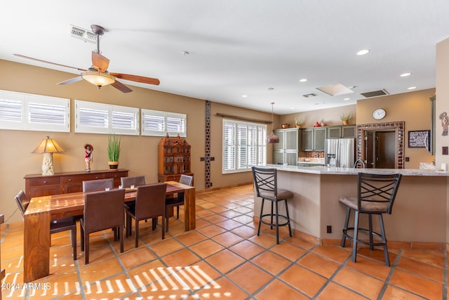 kitchen with light stone countertops, ceiling fan, stainless steel fridge, a breakfast bar area, and light tile patterned floors