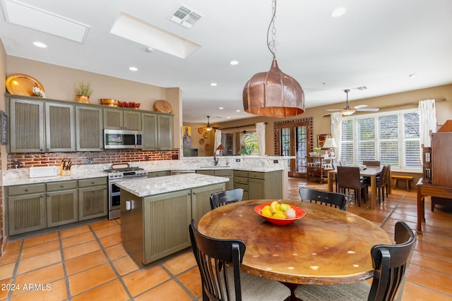 kitchen featuring a skylight, a center island, hanging light fixtures, stainless steel appliances, and kitchen peninsula