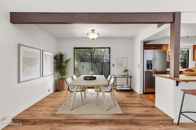 dining room featuring beam ceiling, light wood-type flooring, and a wealth of natural light