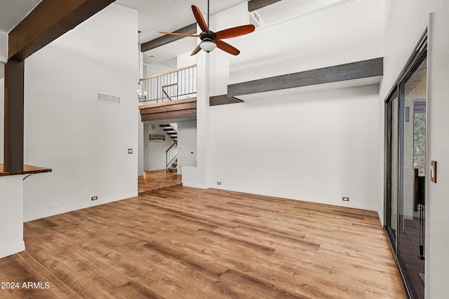 unfurnished living room with beam ceiling, ceiling fan, a towering ceiling, and light wood-type flooring