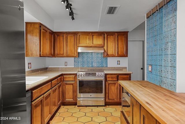 kitchen with sink, rail lighting, appliances with stainless steel finishes, tasteful backsplash, and butcher block counters