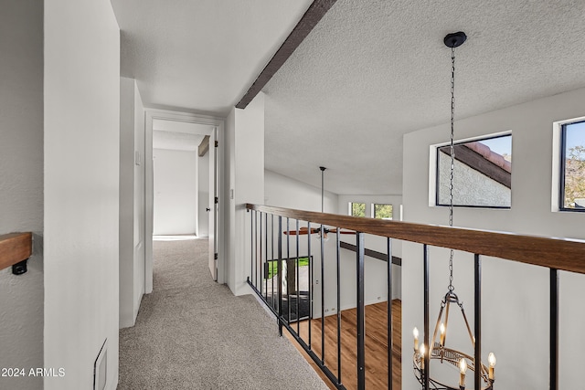 corridor with a notable chandelier, light colored carpet, and a textured ceiling