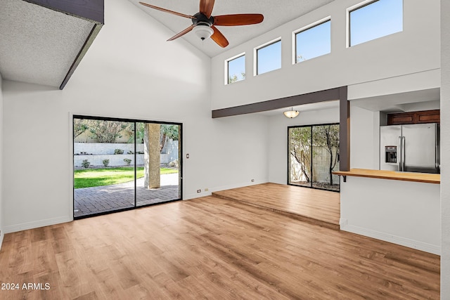 unfurnished living room featuring a textured ceiling, light hardwood / wood-style floors, high vaulted ceiling, and ceiling fan