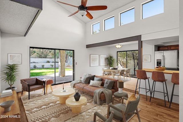 living room featuring ceiling fan, light hardwood / wood-style flooring, high vaulted ceiling, and a healthy amount of sunlight