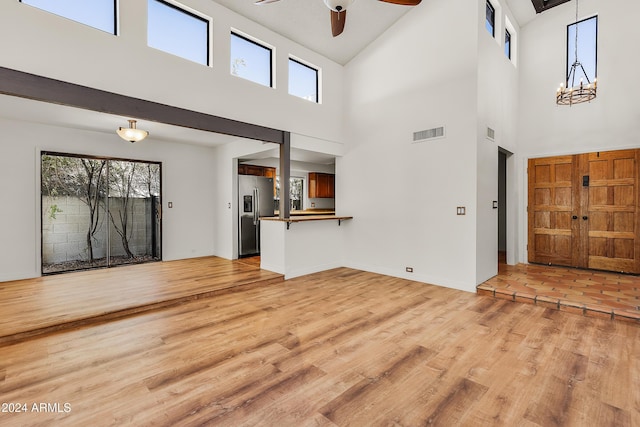 entryway with ceiling fan with notable chandelier, light wood-type flooring, and a towering ceiling