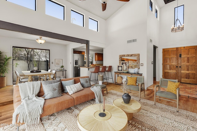 living room with ceiling fan with notable chandelier, light hardwood / wood-style floors, and a high ceiling