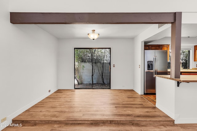 unfurnished dining area with beamed ceiling and light hardwood / wood-style flooring