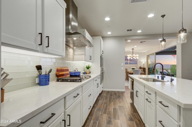 kitchen featuring light stone counters, pendant lighting, sink, stainless steel gas cooktop, and wall chimney range hood