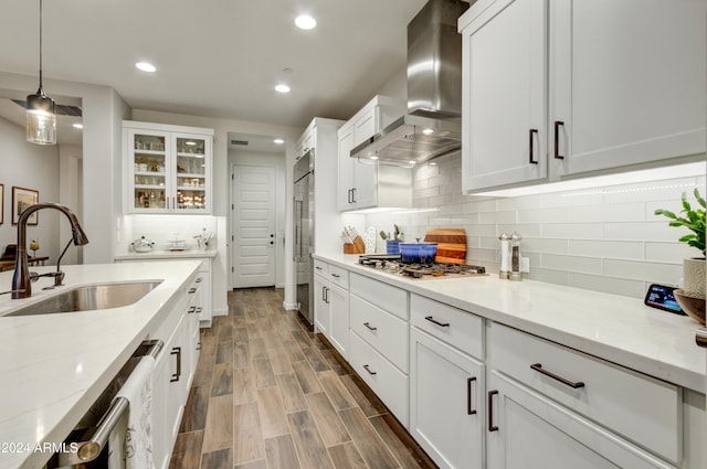 kitchen featuring wood-type flooring, stainless steel appliances, white cabinets, wall chimney exhaust hood, and sink