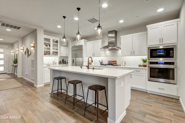 kitchen featuring wall chimney range hood, sink, stainless steel appliances, and light hardwood / wood-style flooring