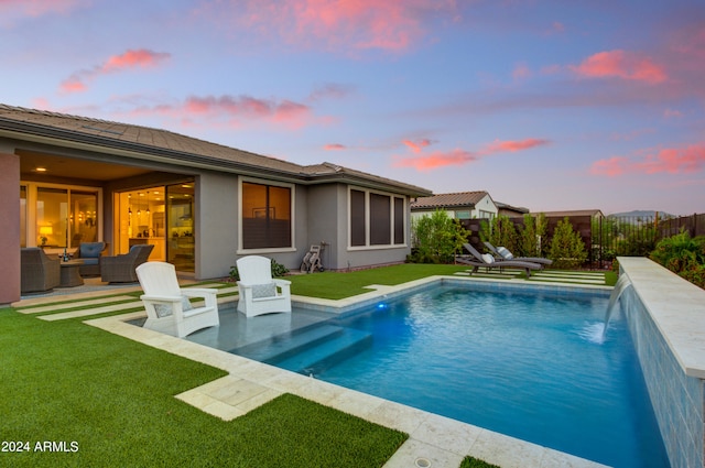 back house at dusk with outdoor lounge area, a fenced in pool, a patio area, pool water feature, and a yard