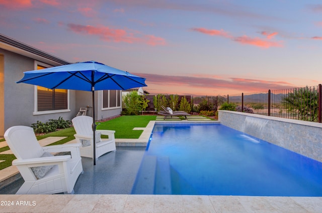 pool at dusk with a yard, a patio area, and pool water feature