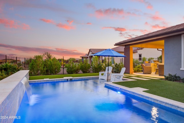 pool at dusk with a yard, pool water feature, and a patio