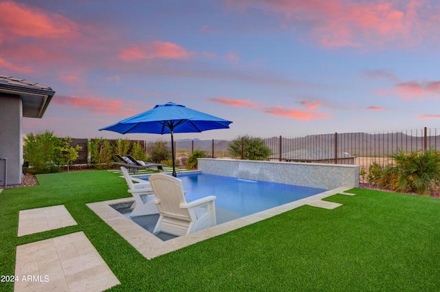 pool at dusk featuring a lawn and pool water feature