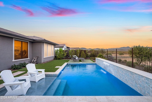 pool at dusk with a patio, a lawn, and pool water feature