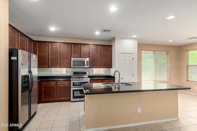 15588 W Devonshire Ave, Goodyear, AZ 85395 - kitchen with appliances with stainless steel finishes, dark countertops, light tile patterned floors, recessed lighting, and a kitchen island with sink