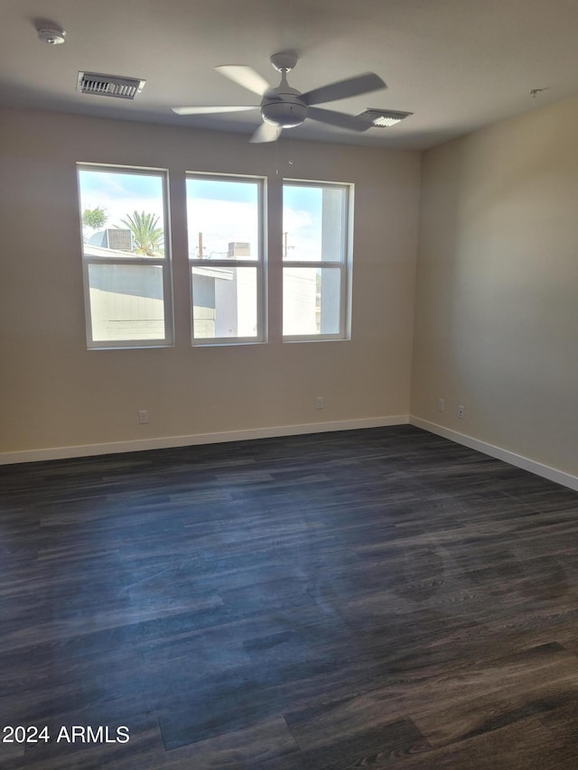 unfurnished room with dark wood-type flooring, a healthy amount of sunlight, visible vents, and baseboards