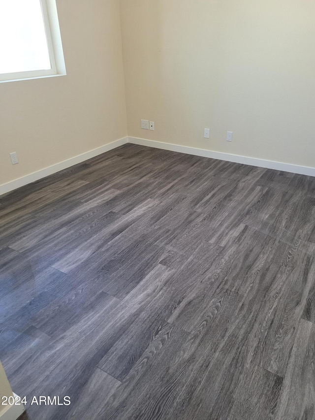 empty room with baseboards and dark wood-type flooring