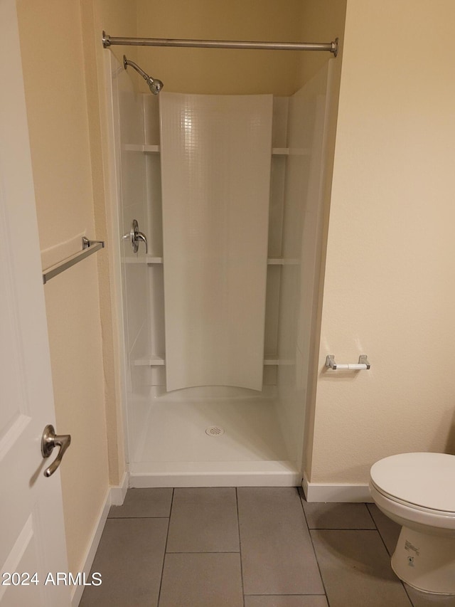 bathroom featuring toilet, a shower stall, baseboards, and tile patterned flooring