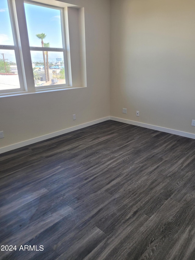 spare room featuring dark wood-style flooring, a wealth of natural light, and baseboards