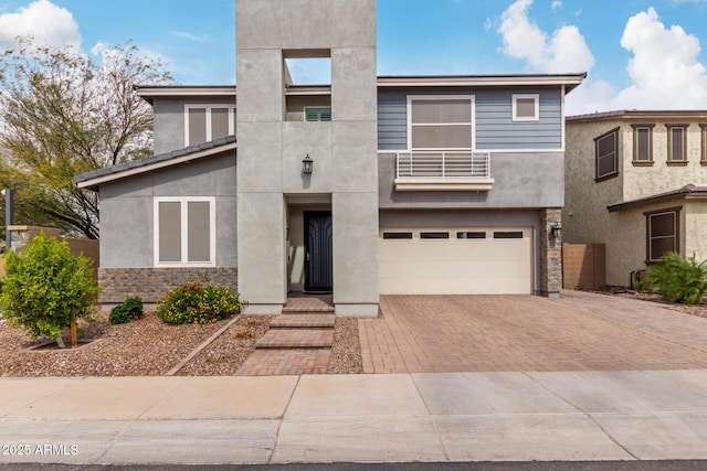 view of front of home featuring a balcony, decorative driveway, an attached garage, and stucco siding