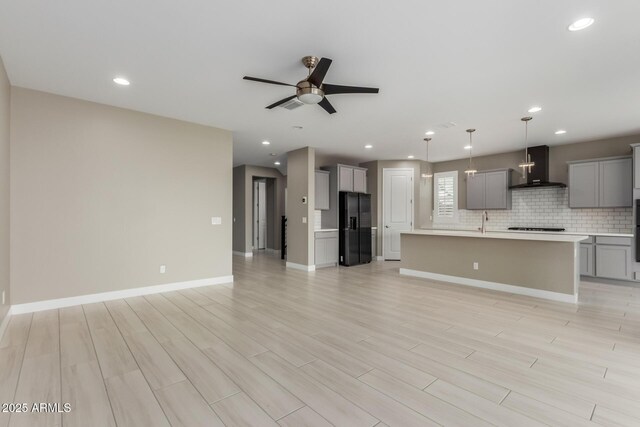 unfurnished living room with a ceiling fan, a sink, recessed lighting, light wood finished floors, and baseboards