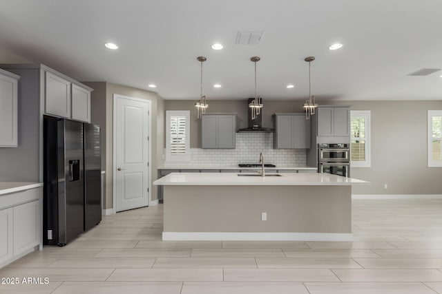 kitchen featuring tasteful backsplash, wall chimney range hood, light countertops, gray cabinets, and stainless steel appliances