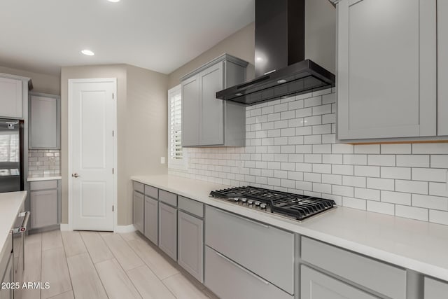 kitchen featuring gray cabinets, backsplash, stainless steel gas stovetop, wall chimney exhaust hood, and light countertops