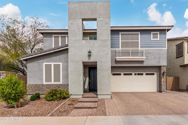 view of front facade with a garage, stucco siding, decorative driveway, and a balcony